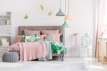 White and pink bedroom interior with leaves drawings hanging above a cozy bed with knit blankets